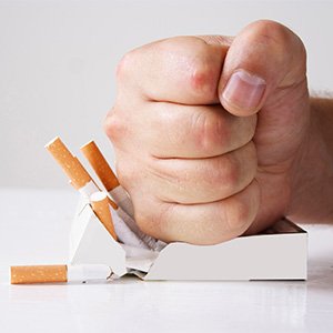 Balled fist crushing a pack of cigarettes on a white surface