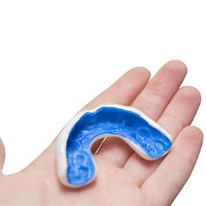 Hand holding a blue and white mouthguard with a white background