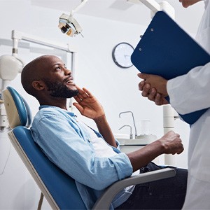 Man in blue shirt in dentist’s chair touching his face with one hand