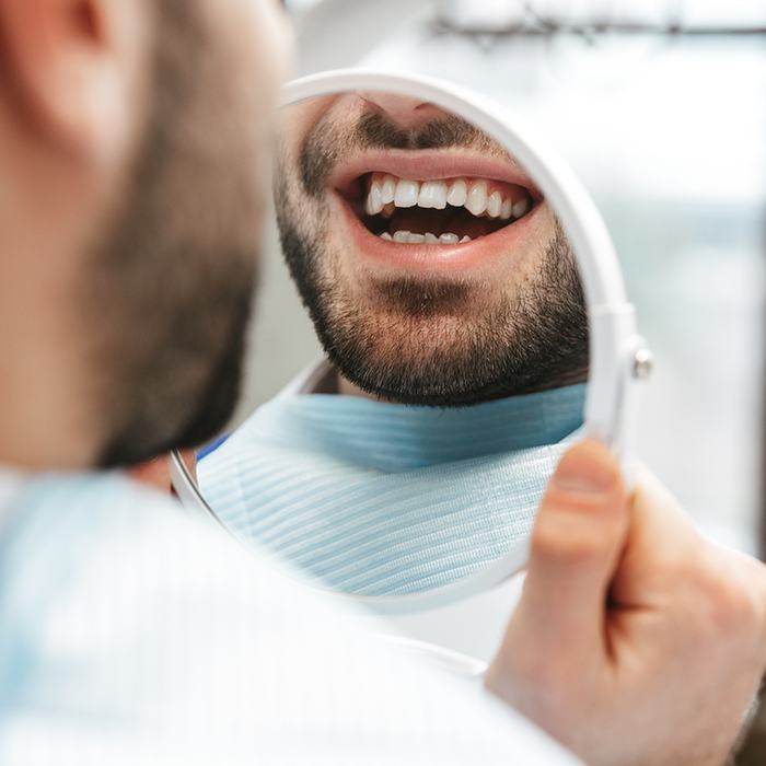 A male dental patient admiring his smile in a hand mirror