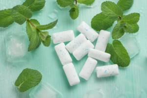 Close up of gum tablets, mint, and ice on blue-green background